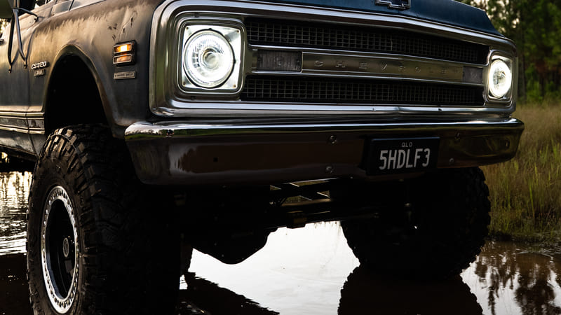 Chevrolet C20 classic pickup truck with off-road suspension and mud-terrain tires, parked in a muddy area.
