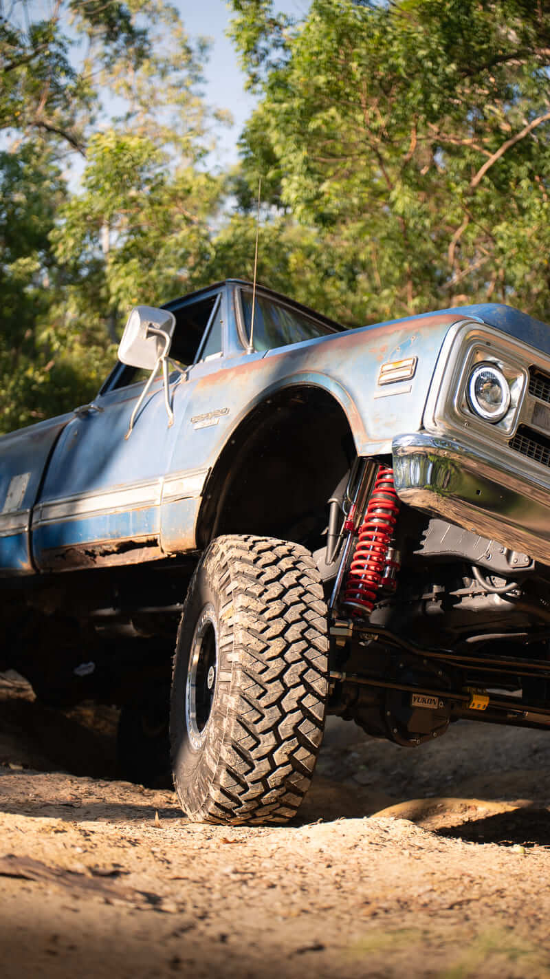 Chevrolet C20 vintage pickup truck with lifted suspension climbing over rough off-road terrain.