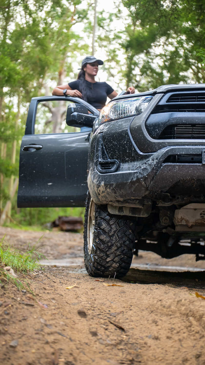 Toyota Hilux 4x4 with all-terrain tires driving through a muddy forest trail.